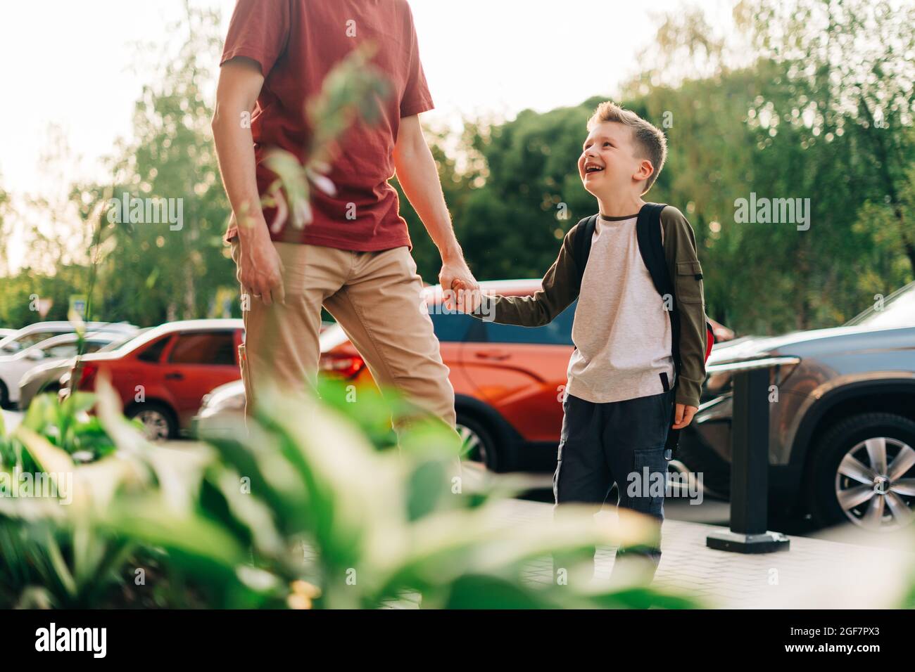 Glücklicher Vater und Kind Sohn gehen in den Unterricht. Eltern nehmen Kind Junge zur Schule in der ersten Klasse. Schüler der Grundschule gehen mit Rucksack im Freien studieren Stockfoto