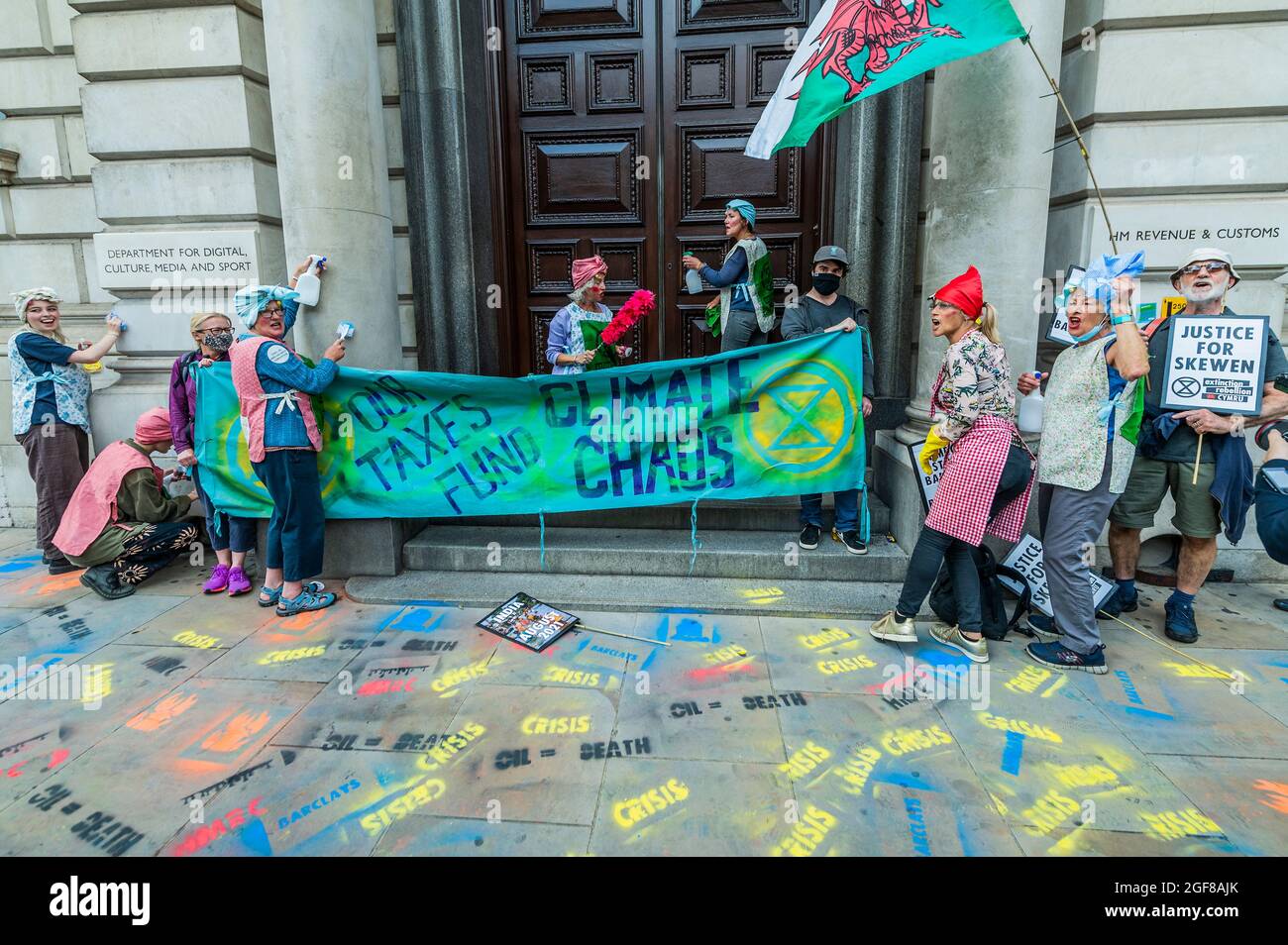 London, Großbritannien. August 2021. Reinigungskräfte kommen, um das Gebäude zu räumen - Anti-Barclays und Anti-Öl-Worte werden vor den Büros des HMRC auf den Bürgersteig gesprüht - XR Cymru protestiert vor HM Revenue and Customs in Whitehall über die Regierungen, die sich mit der fossilen Energiewirtschaft verstrikten und auch Barclays, die sie finanziert haben - Extinction Rebellion Beginnt zwei Wochen lang unter dem Namen Impossible Rebellion in London. Kredit: Guy Bell/Alamy Live Nachrichten Stockfoto