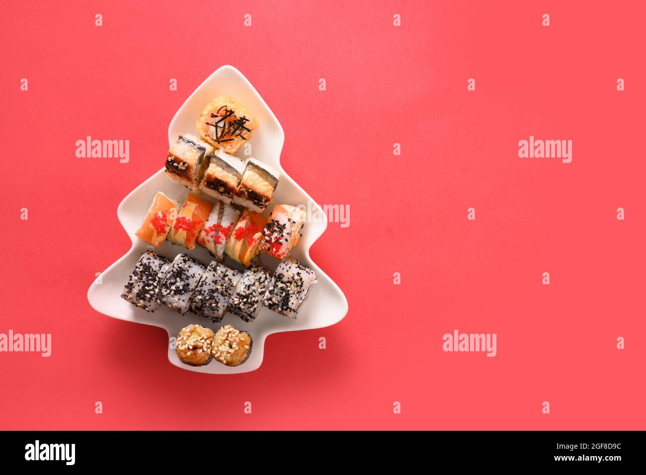 Sushi-Set serviert auf einem Teller als Weihnachtsbaum mit festlicher Dekoration auf rotem Hintergrund. Blick von oben. Stockfoto