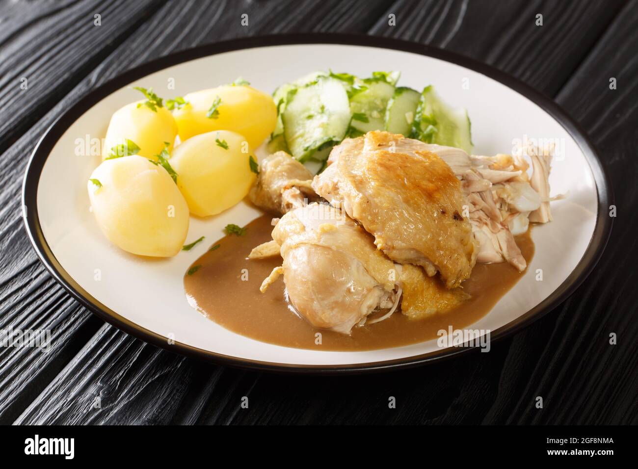 Dänisches gebratenes altmodisches Huhn mit gekochten Kartoffeln und Gurkensalat in Nahaufnahme auf einem Teller auf dem Tisch. Horizontal Stockfoto