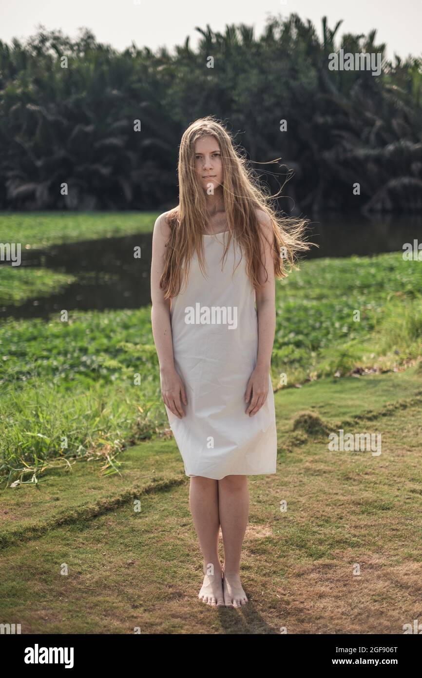 Porträt einer jungen hübschen kaukasischen Frau in weißem Kleid, die im Park steht. Lange blonde Haare. Natürliche Schönheit. Make-up frei. Stockfoto