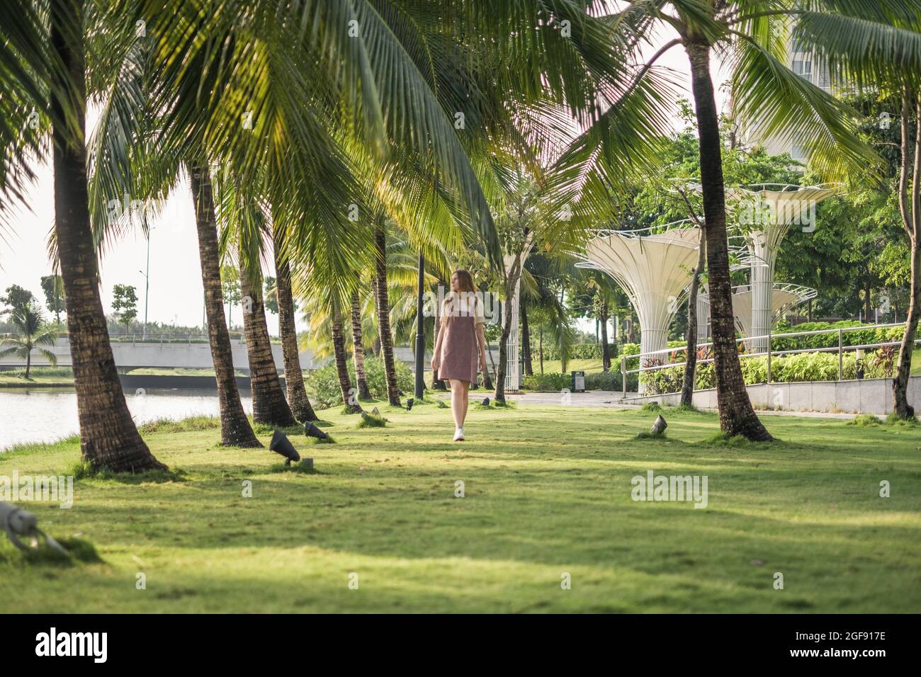 Schöne kaukasische Frau mit langen blonden Haaren zu Fuß im Park mit Palmen. Lässig bequeme Kleidung. Stockfoto