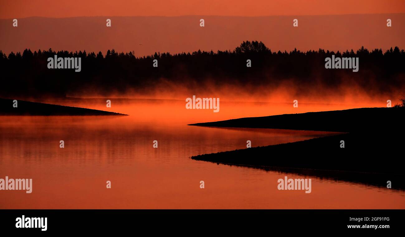 Nebliger Morgen auf dem See mit Dampf, der aus dem Sonnenlicht des Wassers aufsteigt Stockfoto