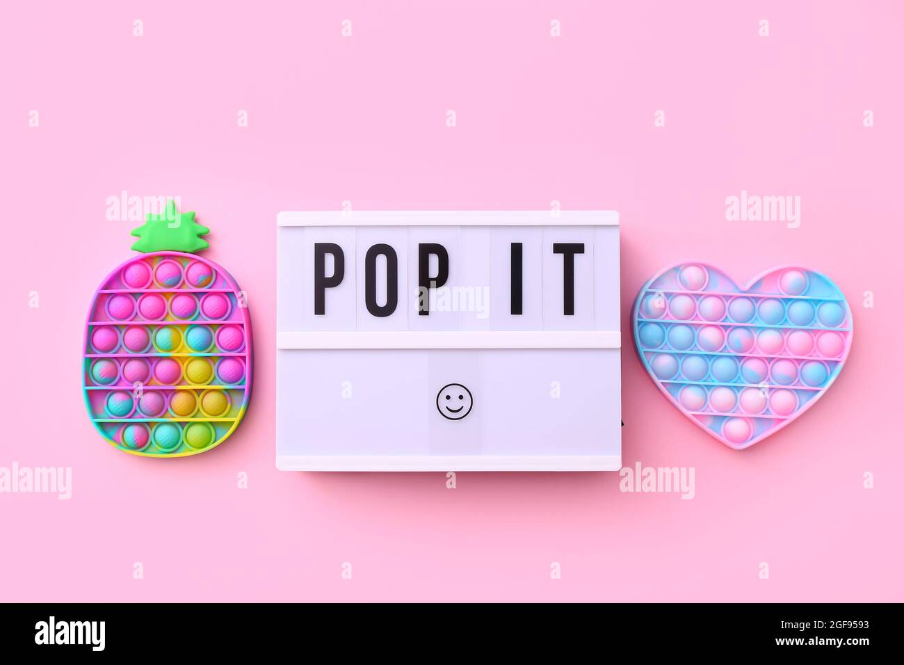 Trendy beliebtes Silikon bunte Anti Stress Pop IT Spielzeug für Kinder auf rosa Hintergrund mit Text Pop IT auf Leuchtkasten. Stockfoto