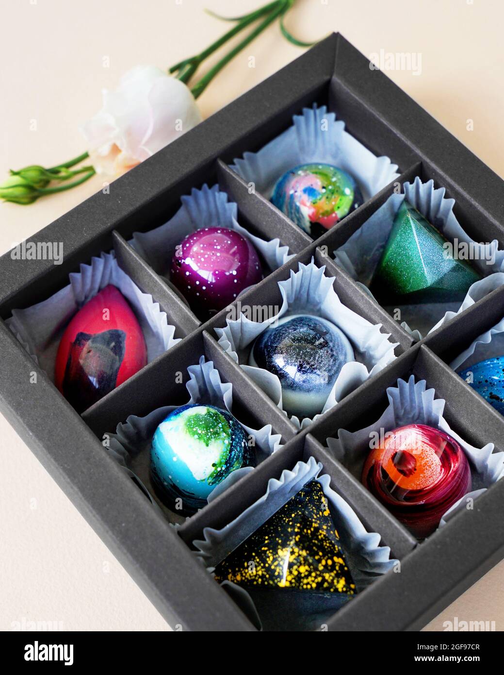Schwarze Geschenkschachtel mit handgefertigten Pralinen. Geometrisches und Raumdesign. Box auf einem hellen Hintergrund. Süßigkeiten und Süßigkeiten aus nächster Nähe Stockfoto