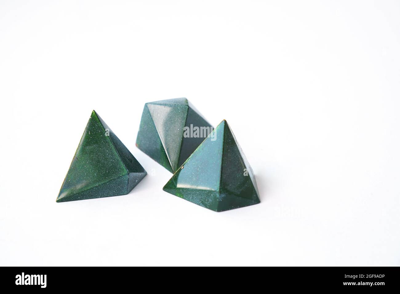 Luxuriöse pyramidenförmige Schokoladenbonbons. Drei Pralinen - grüne Farbe und geometrisches dreieckiges Bonbon-Design. Handarbeit. Isolierte Süßigkeiten auf Weiß Stockfoto