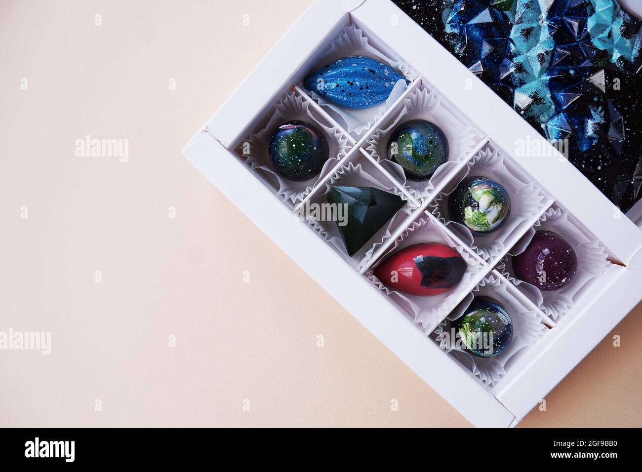 Weiße Geschenkschachtel mit handgefertigten Pralinen. Geometrisches und Raumdesign. Box auf einem hellen Hintergrund. Süßigkeiten und Süßigkeiten aus nächster Nähe Stockfoto