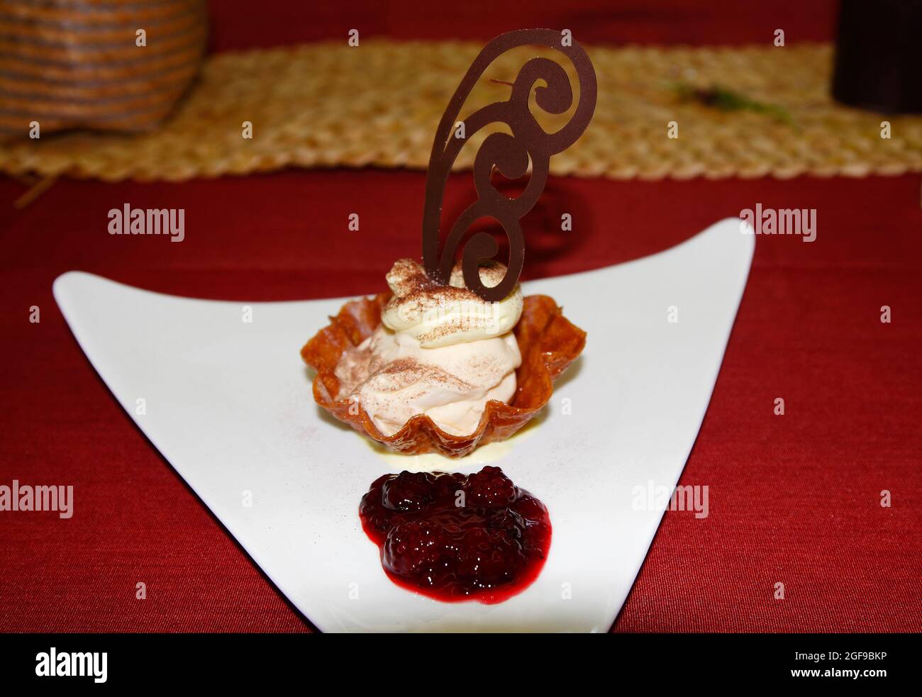 Cremiges Dessert, geriffelter Gebäckbecher, Himbeeren, Schoko-Strudel-Dekoration, süß, Dreieckige weiße Platte, rote Tischabdeckung, attraktiv, Te Puia Maori C Stockfoto