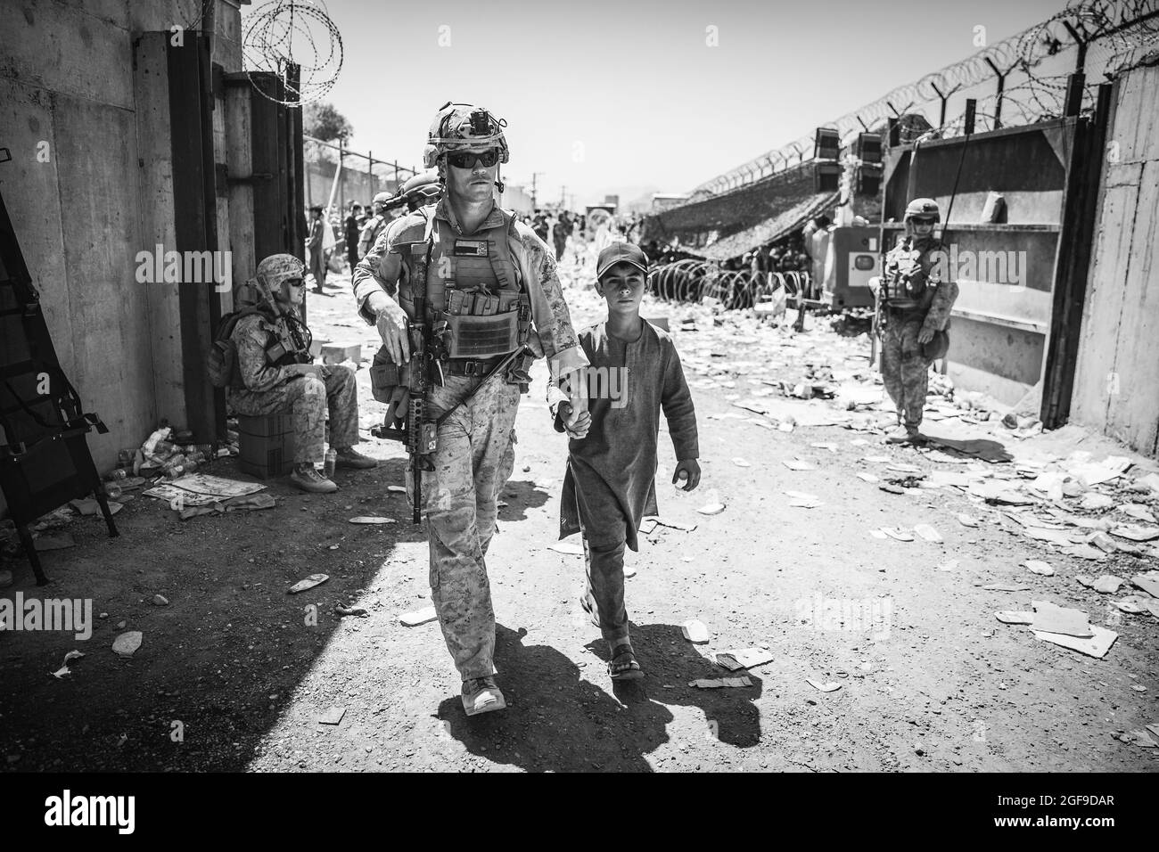 Eine US-Marine mit dem Special Purpose Marine Air-Ground Task Force-Crisis Response-Central Command (SPMAGTF-CR-CC) begleitet ein Kind zu seiner Familie während einer Evakuierung am Hamid Karzai International Airport, Kabul, Afghanistan, August 24. US-Dienstmitglieder und Koalitionsstreitkräfte unterstützen das Außenministerium bei einer nicht-kämpferischen Evakuierungsoperation (NEO) in Afghanistan. (USA Marine Corps Foto von Staff Sgt. Victor Mancilla) Stockfoto