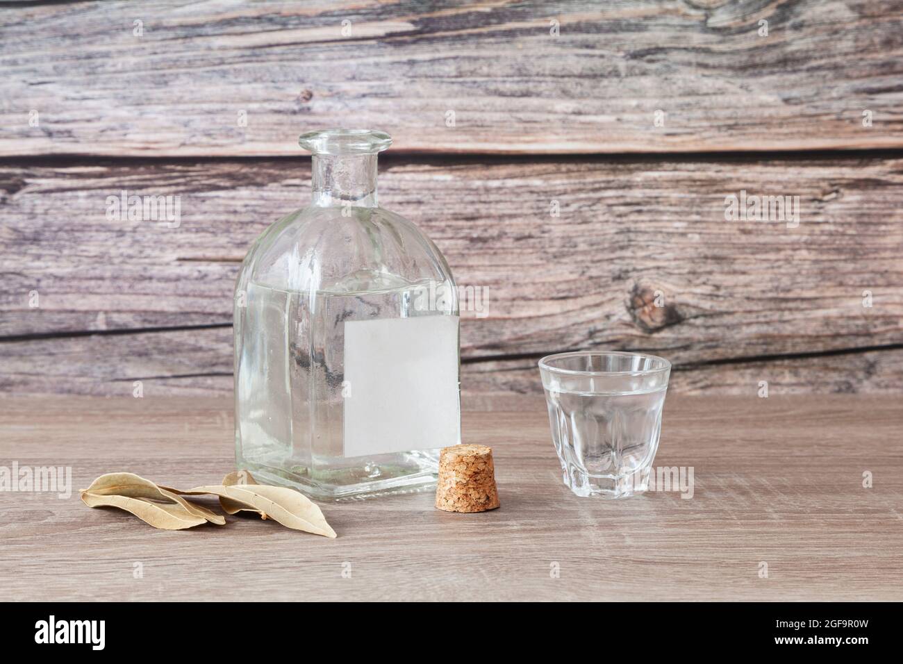 Auf einem Holztisch befindet sich eine ungekorkte Flasche Schnaps mit einem leeren Etikett und einem vollen Schnapsglas. Der Stopfen der Flasche ist neben ihr und es gibt al Stockfoto