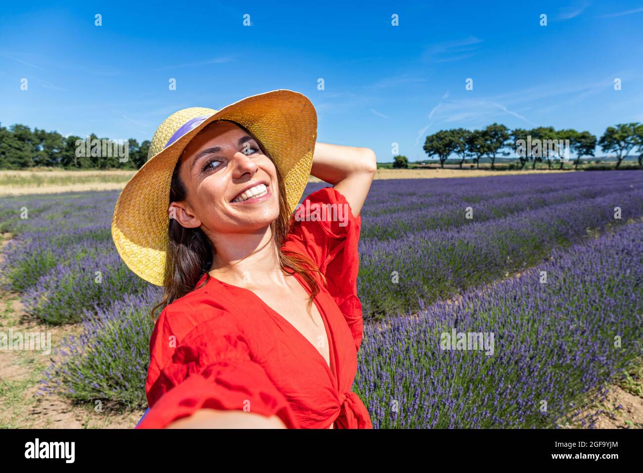 Eine schöne Frau mit Strohhut, die ein Selfie in einem blühenden Lavendelfeld nimmt. Konzept von Glück, Wohlbefinden und Freiheit. Stockfoto