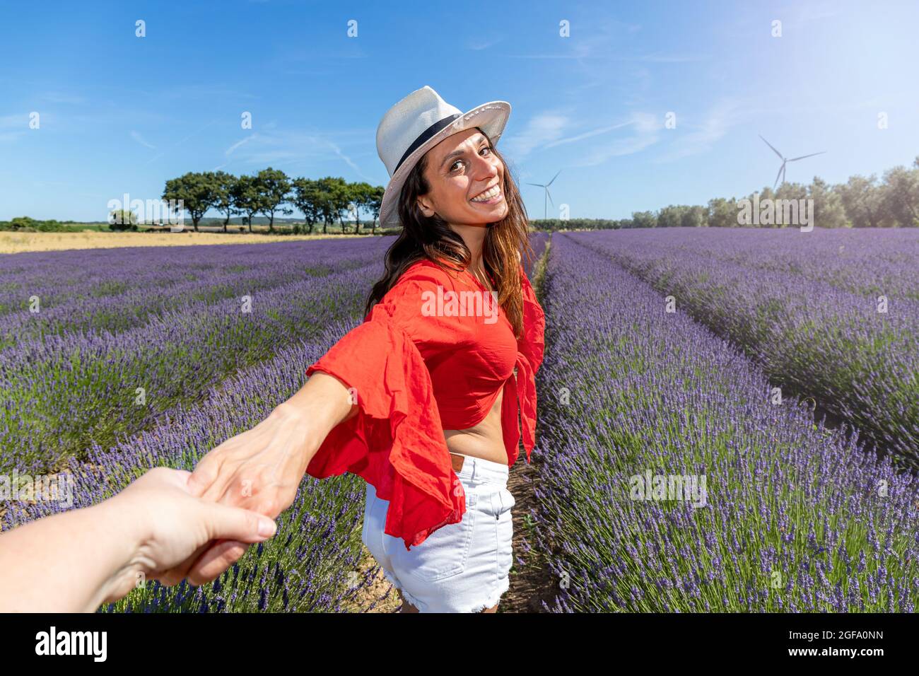 Junge Frau, die in einem Lavendelfeld geht und sich zurückdreht, während sie die Hand einer Person hält. Konzept von Wohlbefinden und Liebe zur Natur. Stockfoto