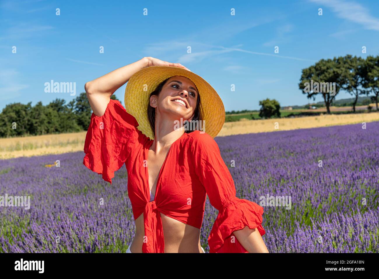 Porträt einer lächelnden jungen Frau, die mit ihrem Strohhut in einem Lavendelfeld spielt. Konzept von Wohlbefinden und Liebe zur Natur. Stockfoto