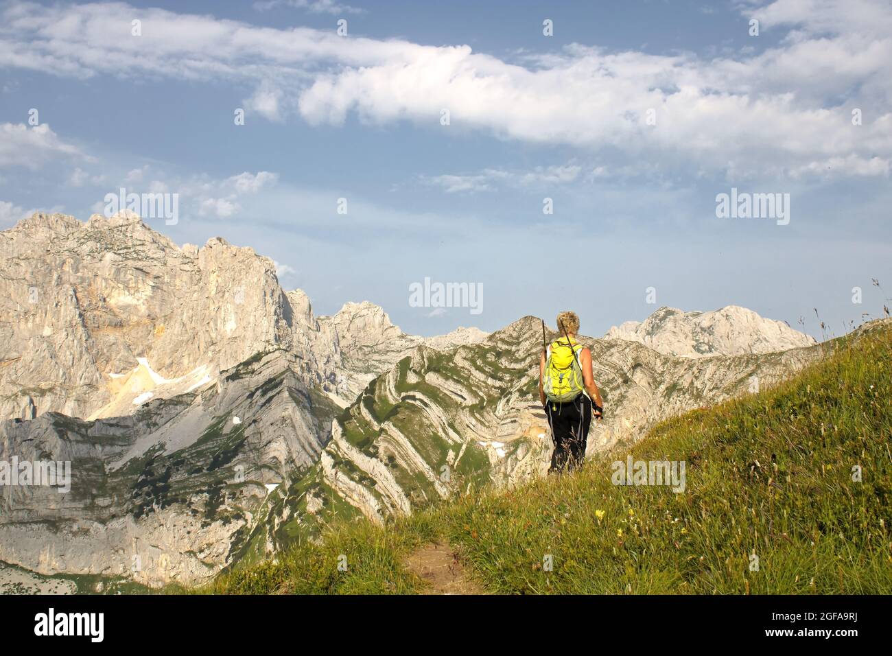 Frau, die auf einem Grasfeld auf felsigen Bergen unter der wolkigen Skyline läuft Stockfoto