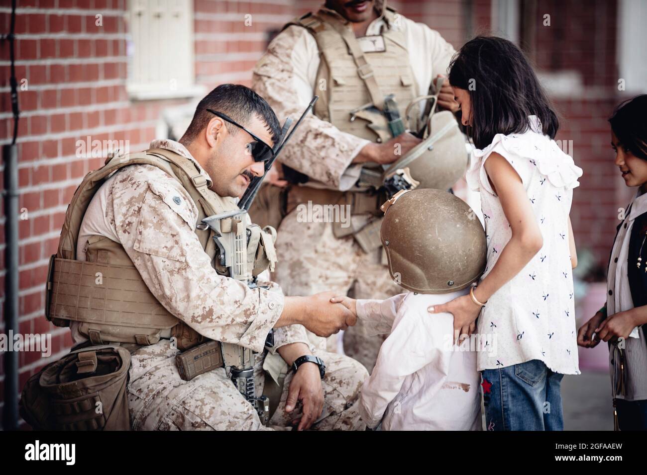 Kabul, Afghanistan. August 2021. Eine US-Marine, die der Special Purpose Marine Air-Ground Task Force zugewiesen wurde - das Krisenreaktionsteam schüttelt sich während der Operation Allies Refuge am 24. August 2021 in Kabul, Afghanistan, die Hände eines Kindes, das seinen Helm trägt, auf dem Hamid Karzai International Airport. Quelle: Planetpix/Alamy Live News Stockfoto