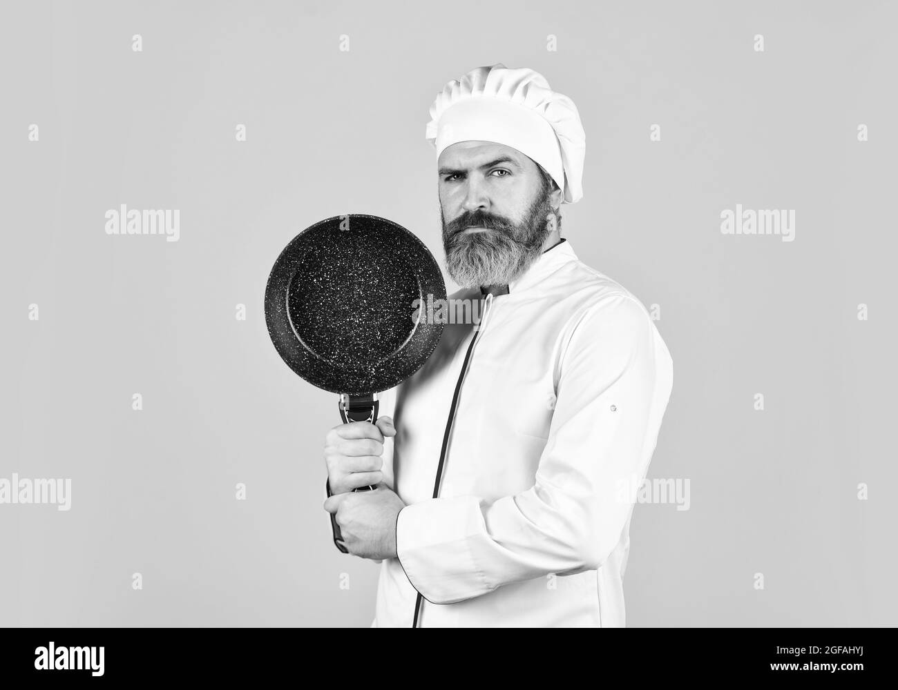 Antihaftbeschichtetes Kochgeschirr. Braten ohne Öl. Professionelle Küchenutensilien. Bärtiger Koch bereitet das Frühstück zu. Antihaftpfanne zum Braten. Emaillierte Kochgefäße Stockfoto