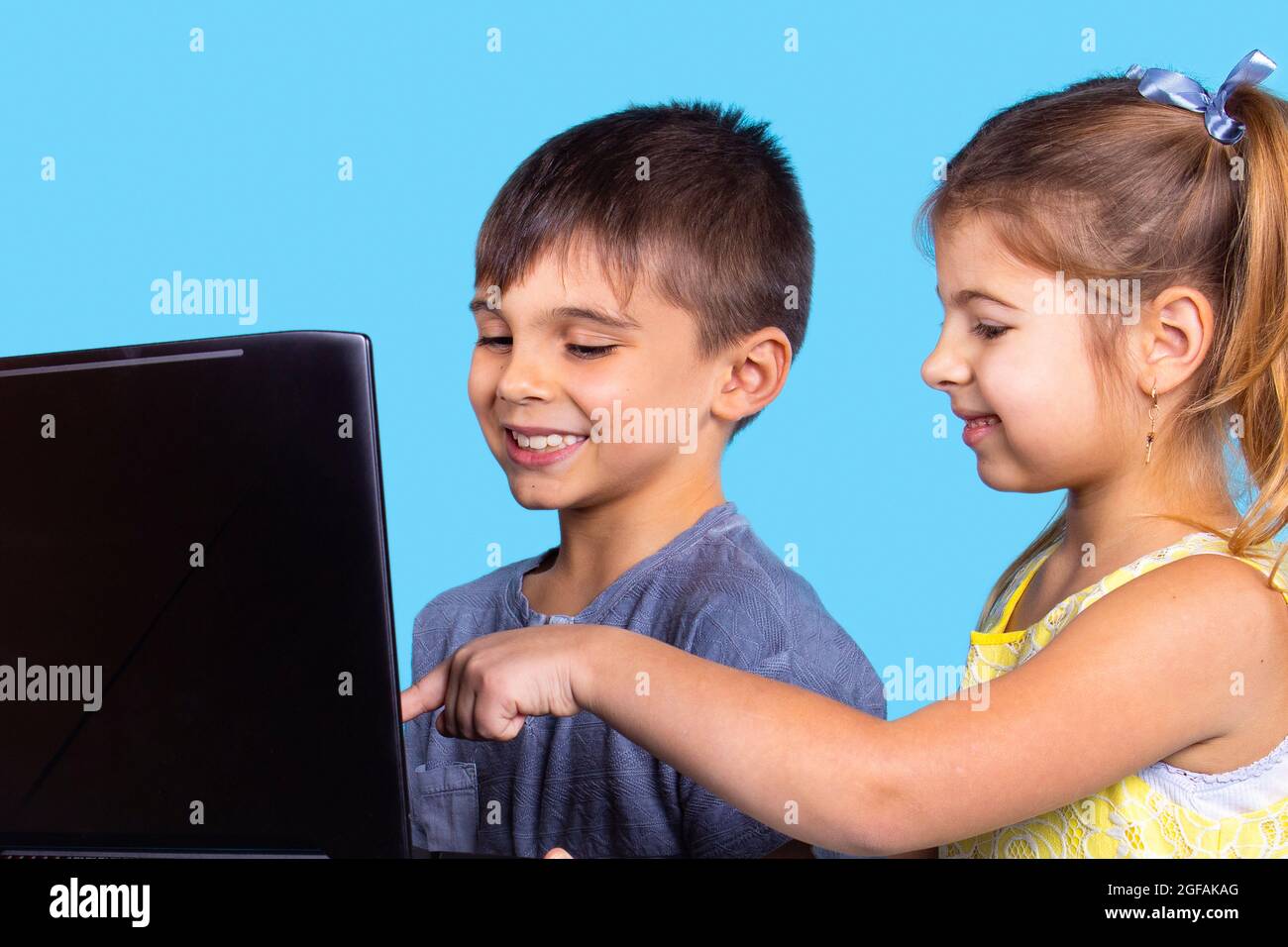 Profilfoto von Schwester und Bruder, die auf den Laptop schauten und zusammen lächelten, wobei das Mädchen mit dem Zeigefinger auf den Laptop-Bildschirm zeigte. Stockfoto