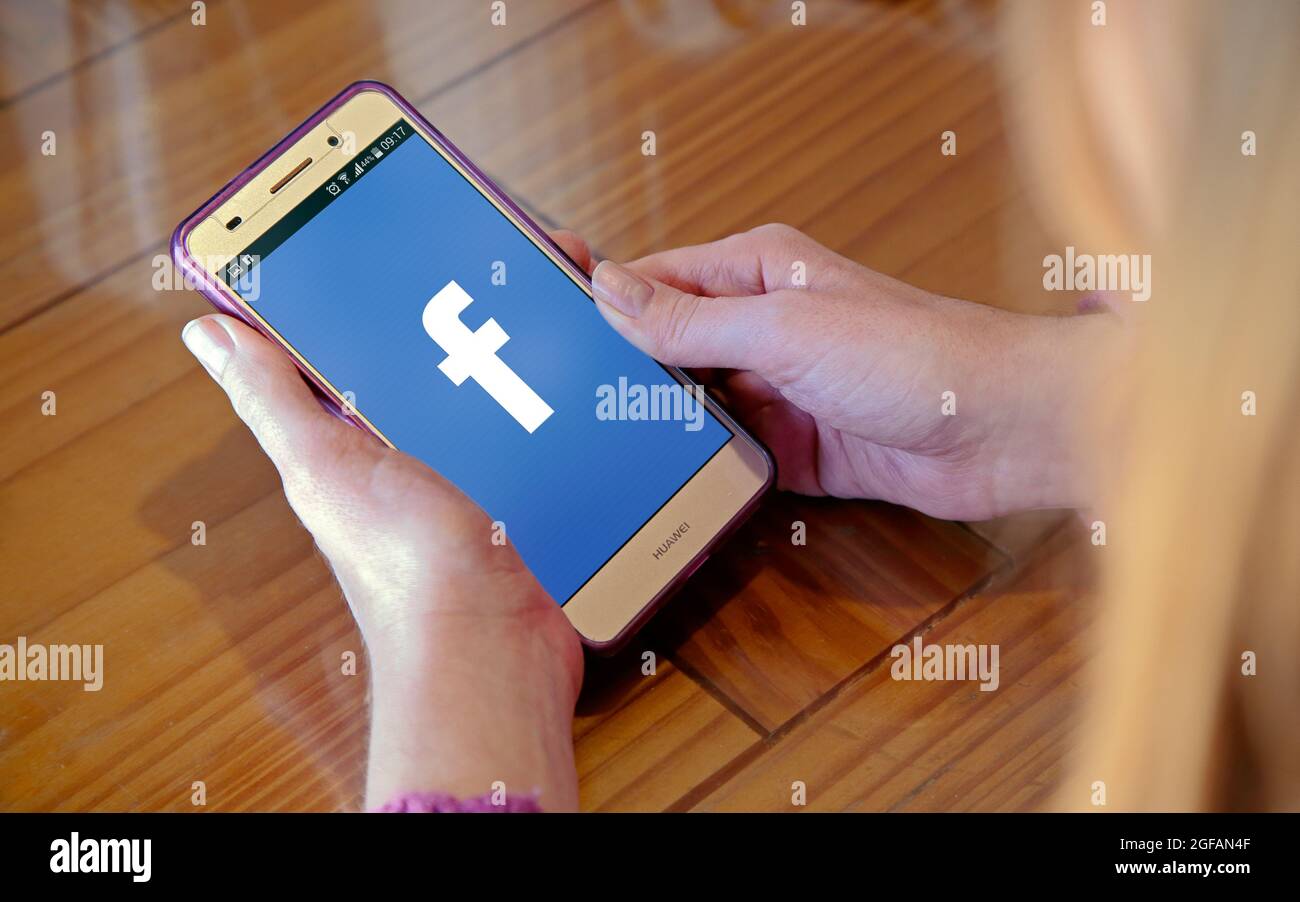 Mädchen mit Handy in den Händen und einem Facebook-Logo auf dem Bildschirm. Junge Frau, tausendjährig. Technologie. Soziales Netzwerk. Stockfoto