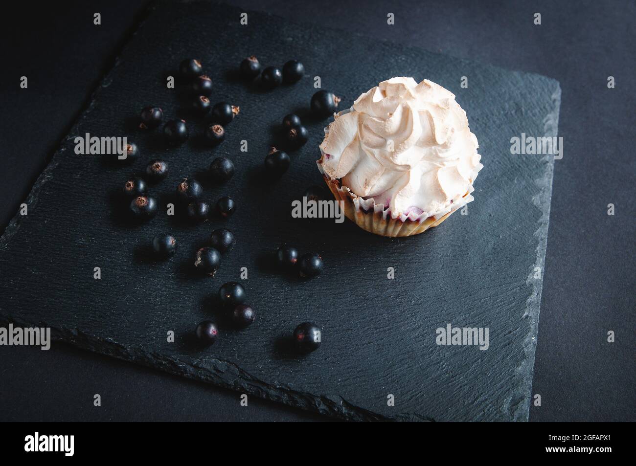 Muffin auf schwarzem Hintergrund mit Johannisbeeren. Auf dunklem Hintergrund Kuchen mit Fruchtfüllung und Beeren und Johannisbeeren auf einem schwarzen Stein serviert bo Stockfoto