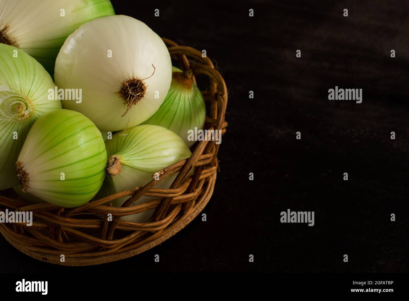 Einige große grüne Zwiebeln zum Kochen in einem braunen Korb auf einem schwarzen Tisch mit Platz zum Kopieren Stockfoto