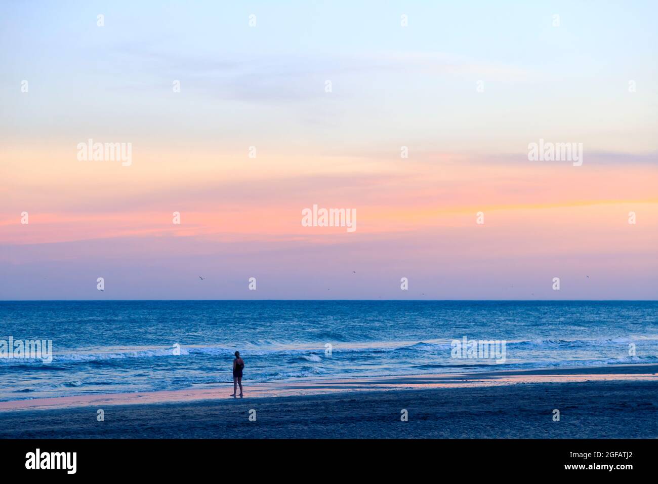 Junge Frau am Strand, die beim Sonnenuntergang das Meer beobachtet. Mar de las Pampas, Buenos Aires, Argentinien. Inspirierendes Bild. Stockfoto