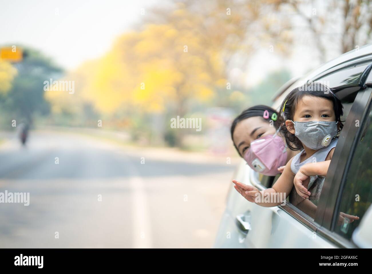 Mutter und Tochter haben Spaß beim Reiten auf der Rückseite eines Autos, während sie eine Schutzmaske tragen Stockfoto