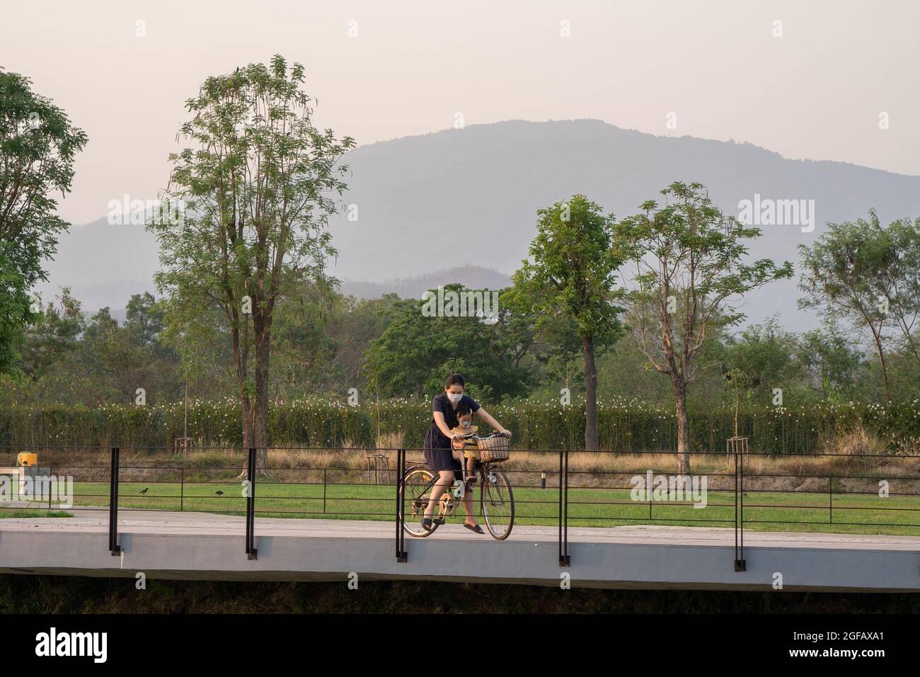 Mutter und Tochter reiten auf einem Fahrrad in einem Park, während sie eine Schutzmaske tragen Stockfoto