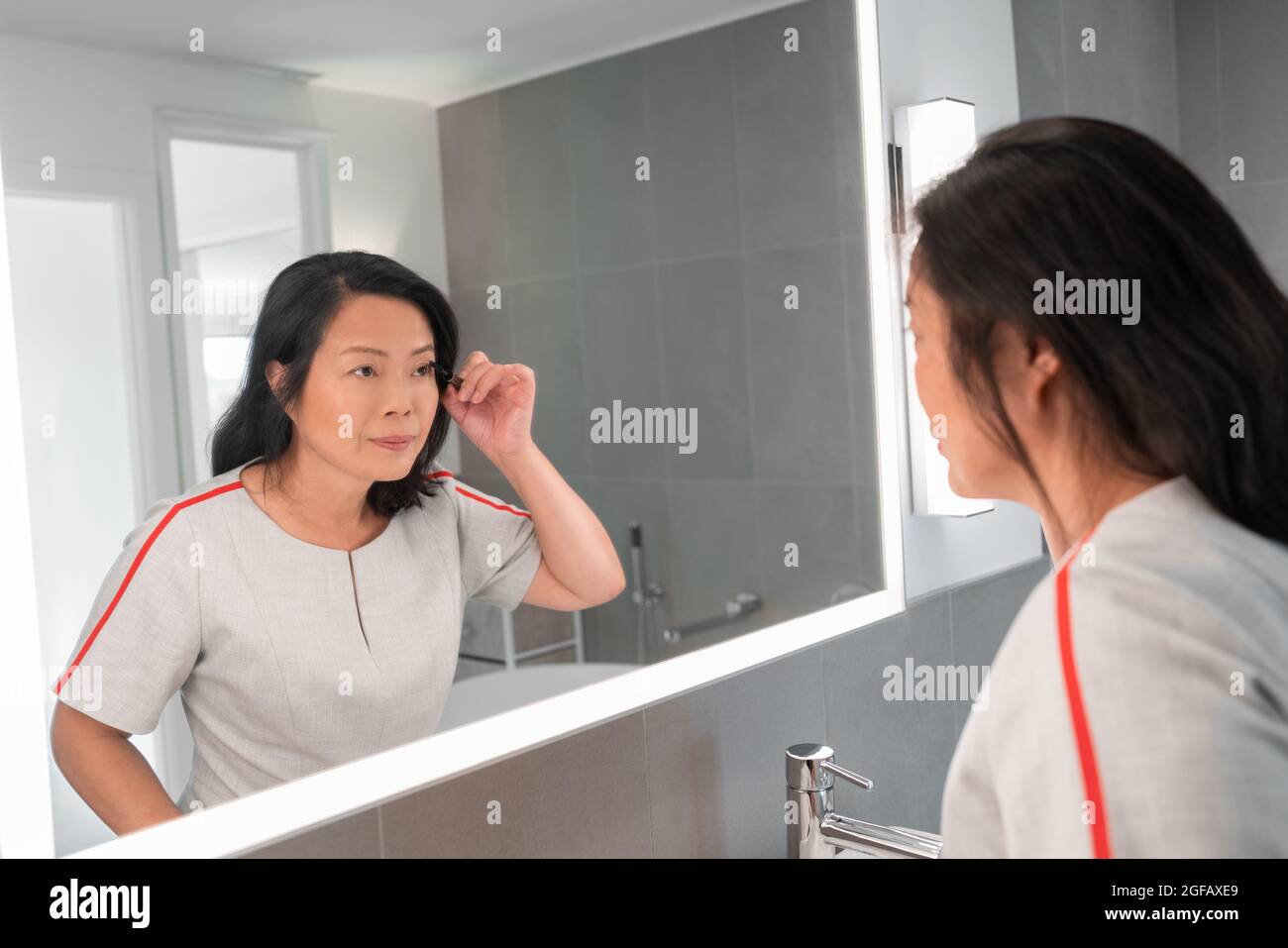 Asiatische reife Frau Putting Mascara suchen in LED-Lichtrahmen Spiegel Anwendung Make-up immer bereit für die Arbeit zu Hause Badezimmer. Chinesische ältere Dame Stockfoto