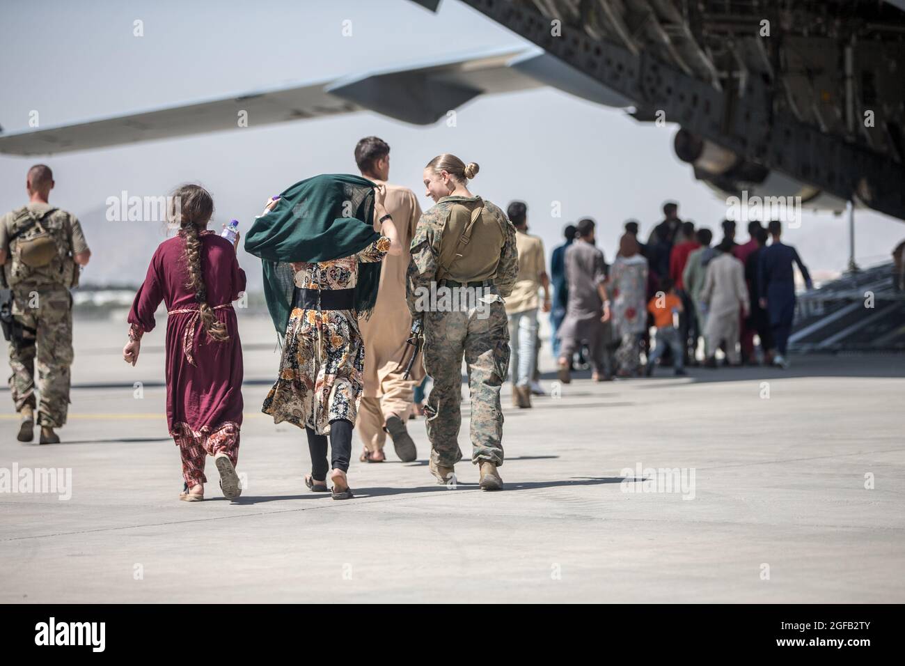 Eine Marine mit der 24. Marine Expeditionary Unit (MEU) geht mit den Kindern während einer Evakuierung am Hamid Karzai International Airport, Kabul, Afghanistan, August 24. US-Dienstmitglieder unterstützen das Außenministerium bei einer geordneten Abseichung von designiertem Personal in Afghanistan. (USA Marine Corps Foto von Sgt. Samuel Ruiz). Stockfoto