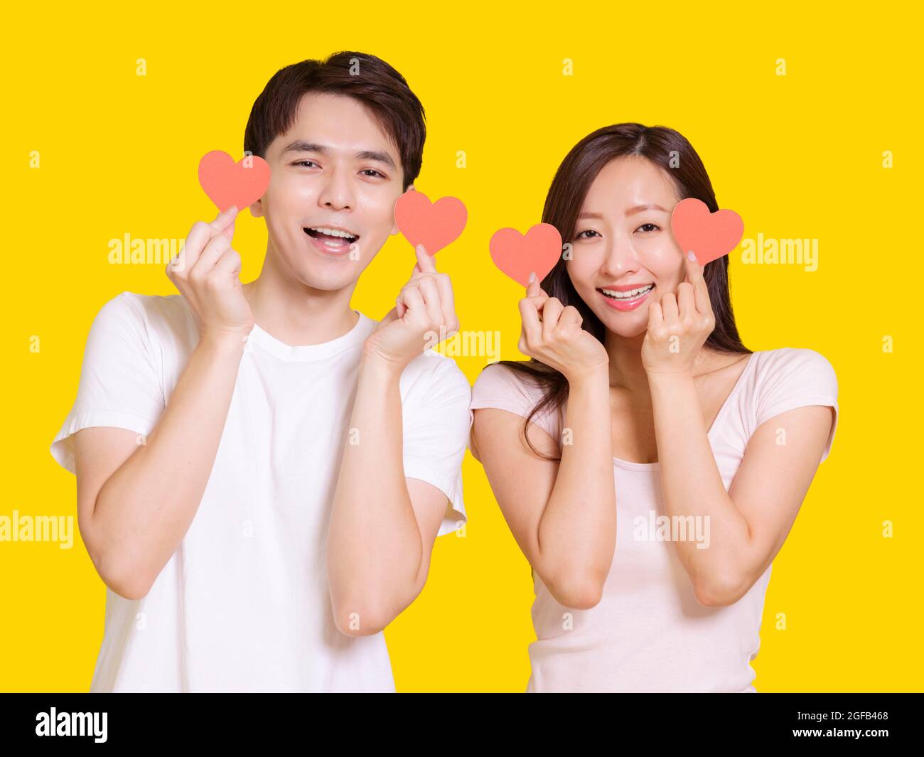 Junges Paar zeigt rote Herzen Form .isoliert auf gelbem Hintergrund. Stockfoto
