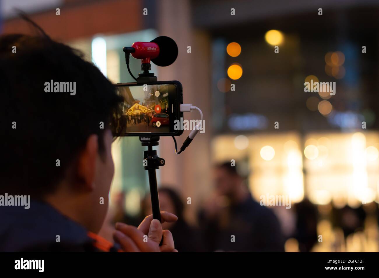 Content Creator, der durch den Weihnachtsmarkt von Manchester geht und ein mit dem Pixel 4 aufzeichnendes Video mit dem Mikrofon von Salto für vlog aufzeichnet. Stockfoto