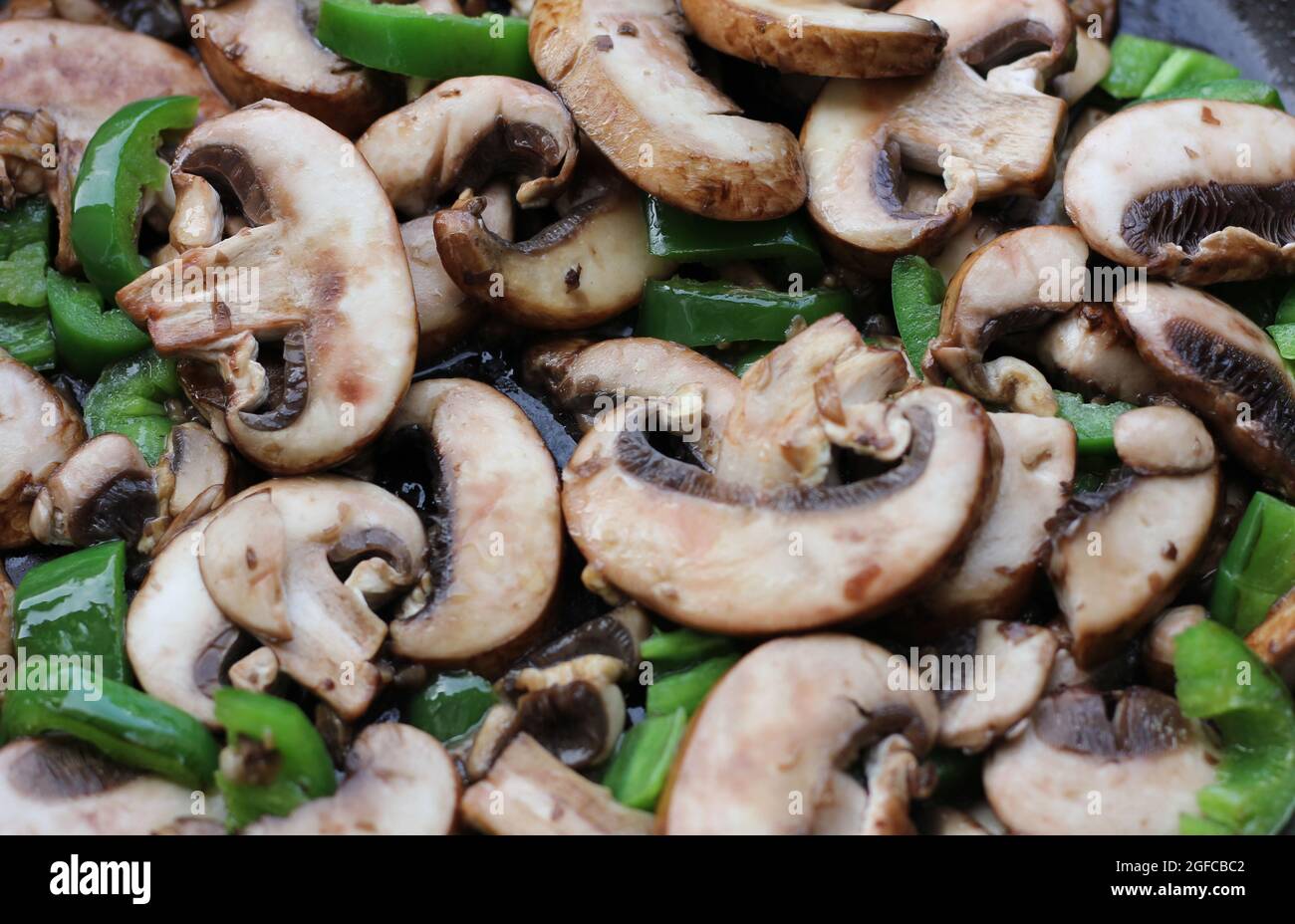 Geschnittene Pilze und gehackte grüne Paprika Kochen in Pfanne Close Up Stockfoto