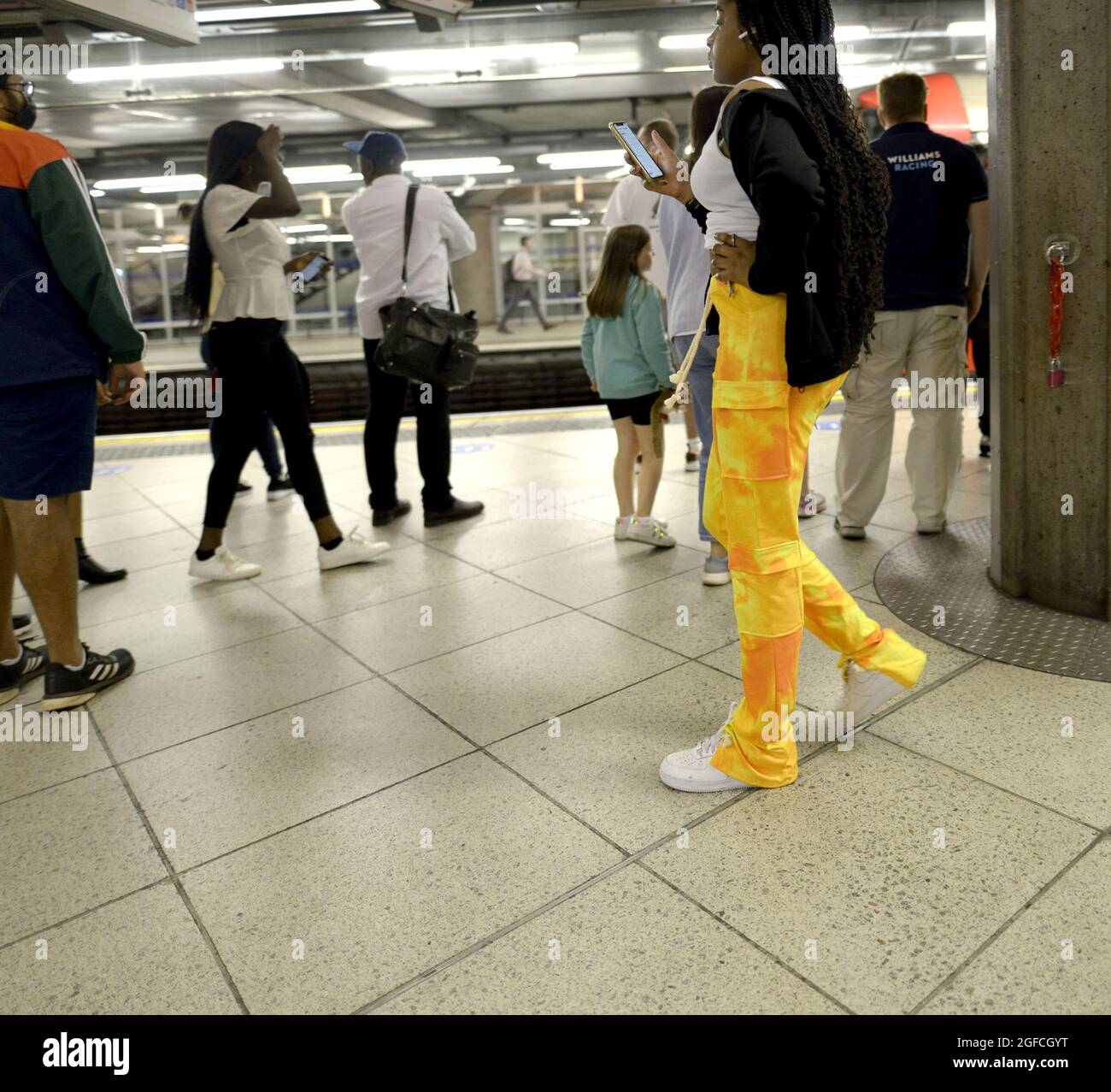 London, England, Großbritannien. U-Bahn-Station. Junge schwarze Frau trägt eine leuchtend gelbe Hose auf ihrem Mobiltelefon Stockfoto