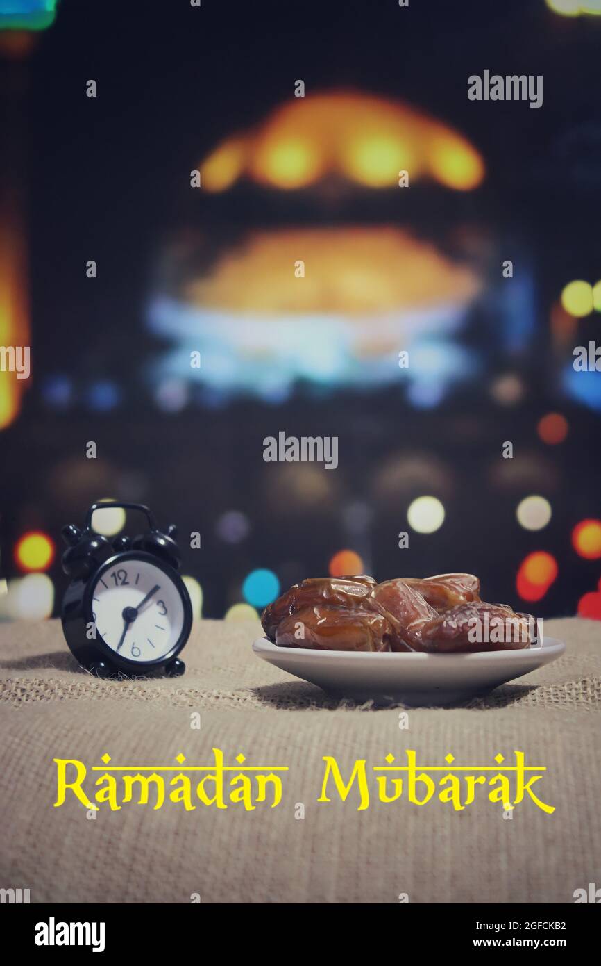 Konzept des Fastenmonats Ramadan. Selektives Fokusbild von Datteln, Obst und Wecker. Bokeh-Effekt Moschee im Hintergrund. Stockfoto