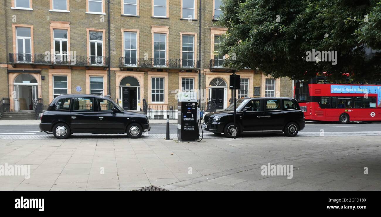 Ein herkömmliches Dieseltaxi neben einem schwarzen Elektrotaxi, das sich in London selbst lädt Stockfoto