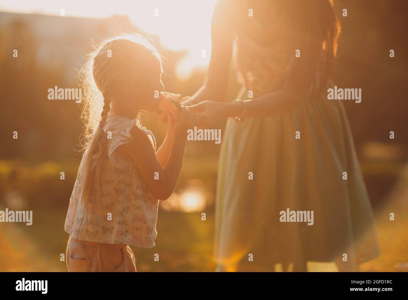 Mutter füttert Mädchen mit Wassermelone im Park mit Lichtreflexe. Sommer, Park, Aktivitäten Außen, Familienleben. Stockfoto