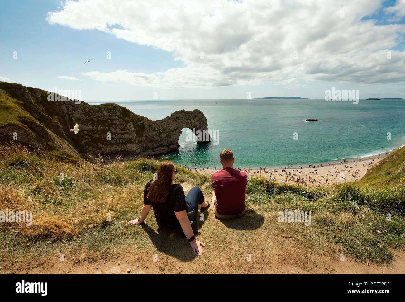 Durdle Door, die ikonischste Landschaft der Jurassic Coast mit ihrem natürlichen Kalksteinbogen. Junges Paar genießt einen sonnigen Sonntag. Dorset, Großbritannien. 22 August 2021 Stockfoto