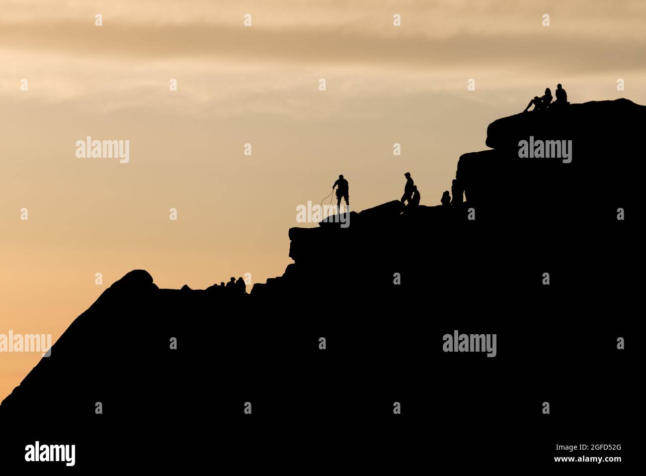 Dramatische Silhouette-Szene, in der ein Kletterer seine Seile an der Spitze einer markanten Felsformation sortiert. Andere Menschen genießen den Sonnenuntergang und die abgelegene Wildnis. Stockfoto