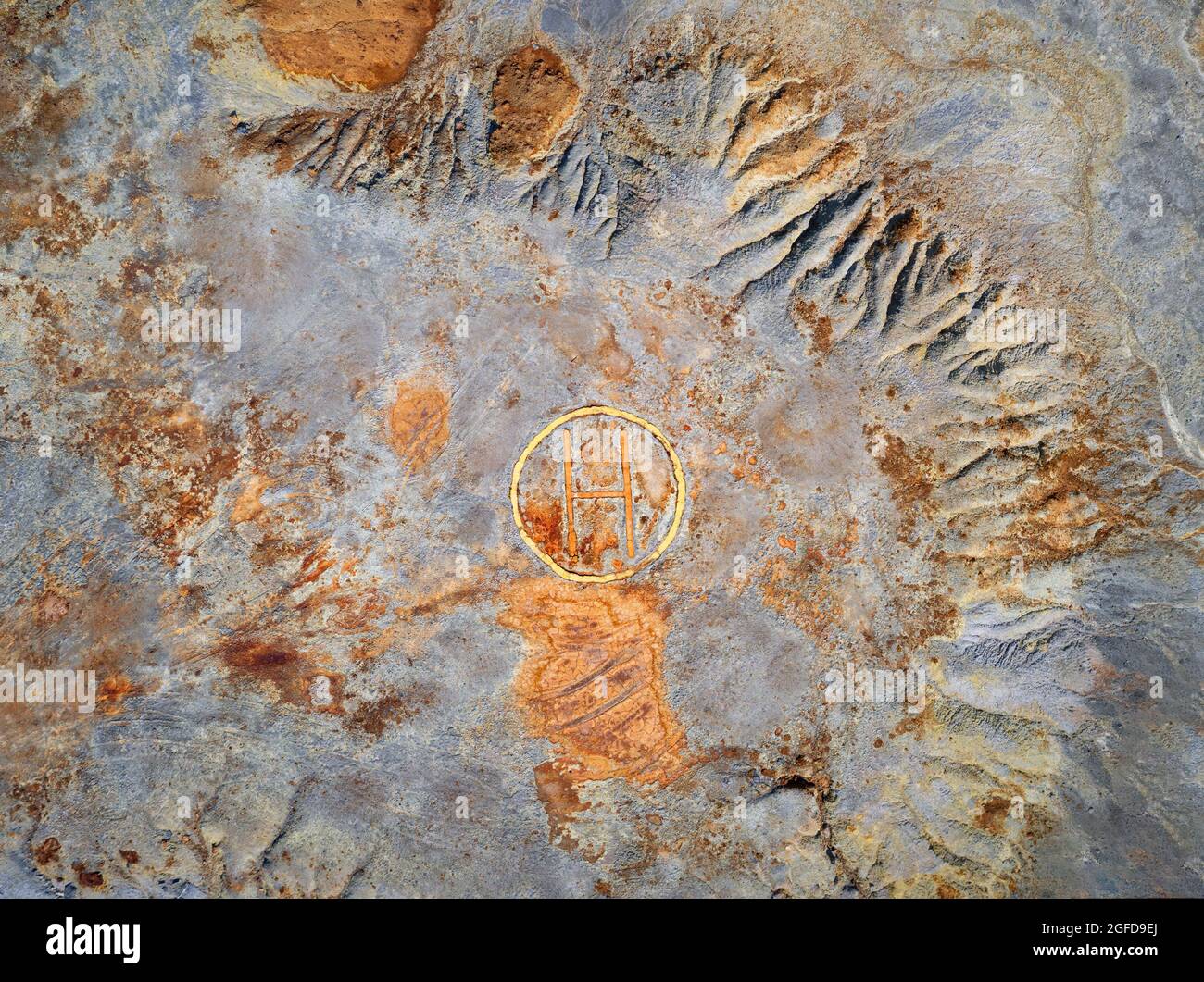 Verlassene Bergrückstände mit Hubschrauberlandeplatz und bunten rostigen Flecken auf grauer, rauer Oberfläche. Industrielle Texturansicht von oben Stockfoto