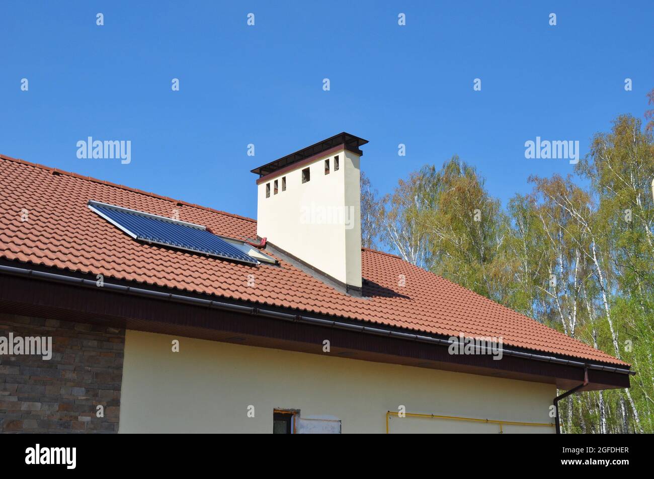 Eine Nahaufnahme des Lehmdachs eines energieeffizienten Einfamilienhauses mit solarem Warmwasserheizpanel, einem Dachfenster, einem Kamin und einer Regenrinne Stockfoto