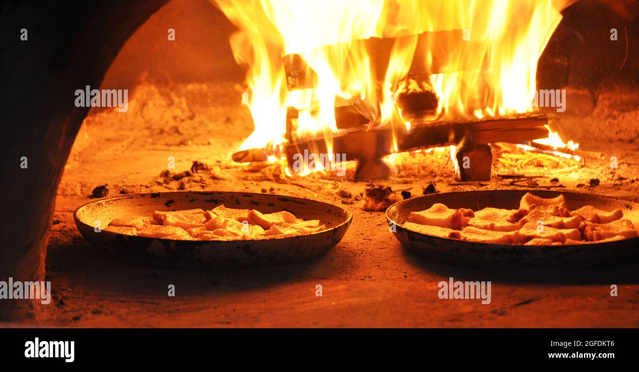 Kochen ukrainischer traditioneller Gerichte in einem Holzofen, Braten von Fleisch, fatback-Schweinefleisch vor einer heißen Feuerflamme in einem Steinofen. Stockfoto