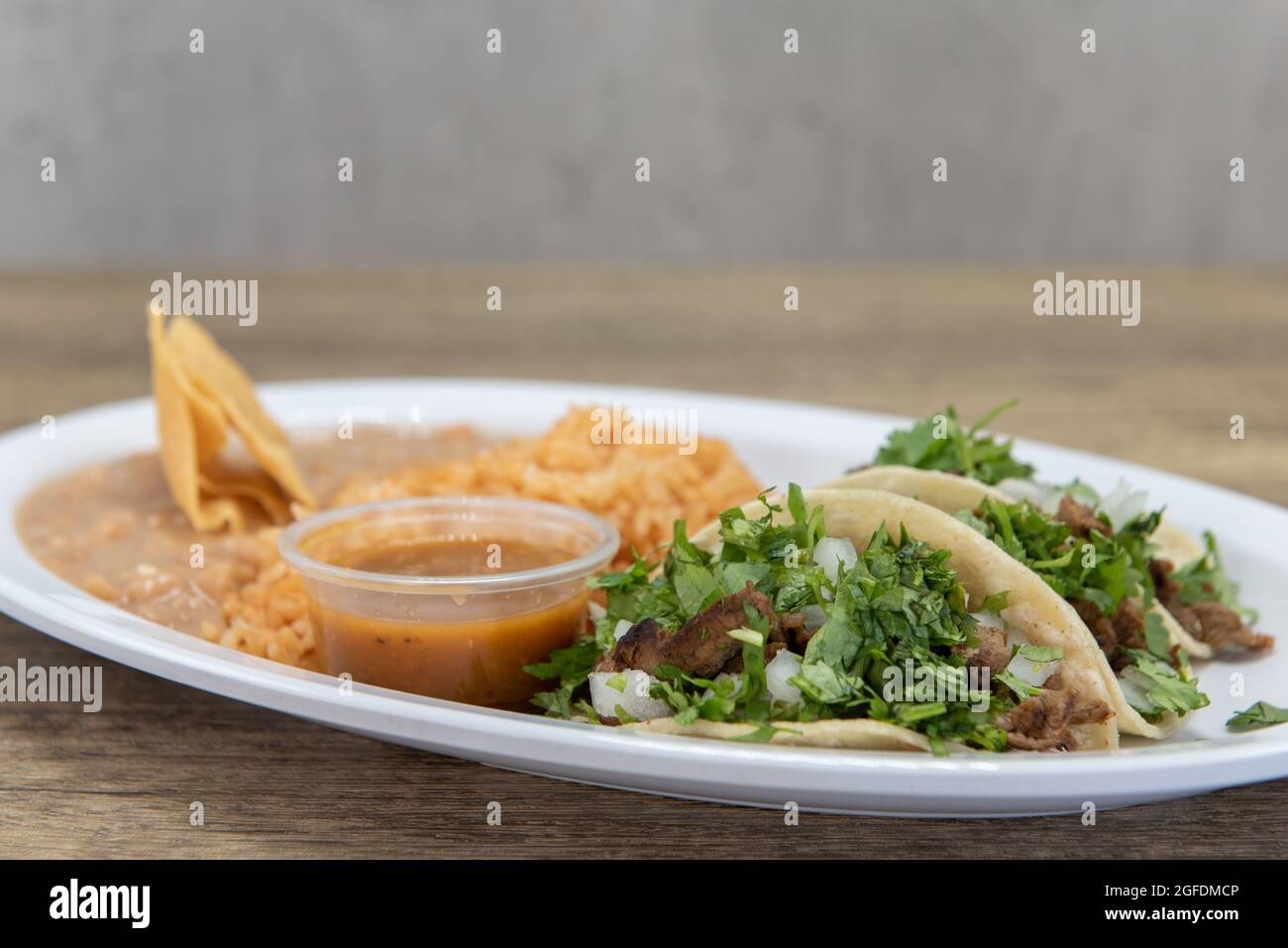 Herzhafte Platte mit drei geladenen Carne Asada Tacos mit Koriander, serviert mit Reis und gebratenen Bohnen. Stockfoto