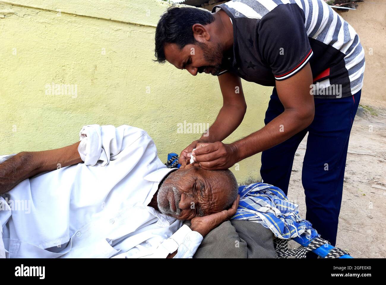 Ein ländlicher Jugendlicher, der seinem kränkelnden Großvater Medizin ins Ohr gießt, ländliche Umgebung. Stockfoto