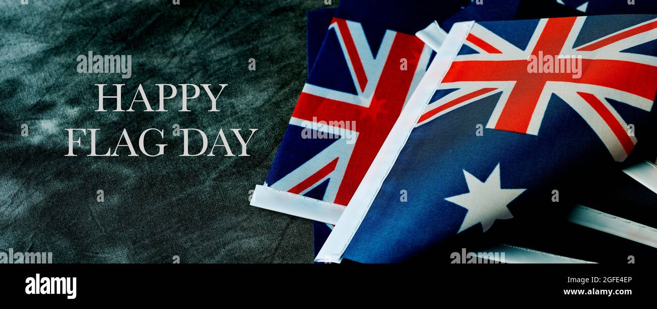 Nahaufnahme einiger australischer Flaggen und des Textes Happy australia Day auf dunkelgrauem Hintergrund, in einem Panoramaformat, das als Webbanner oder Header verwendet werden kann Stockfoto