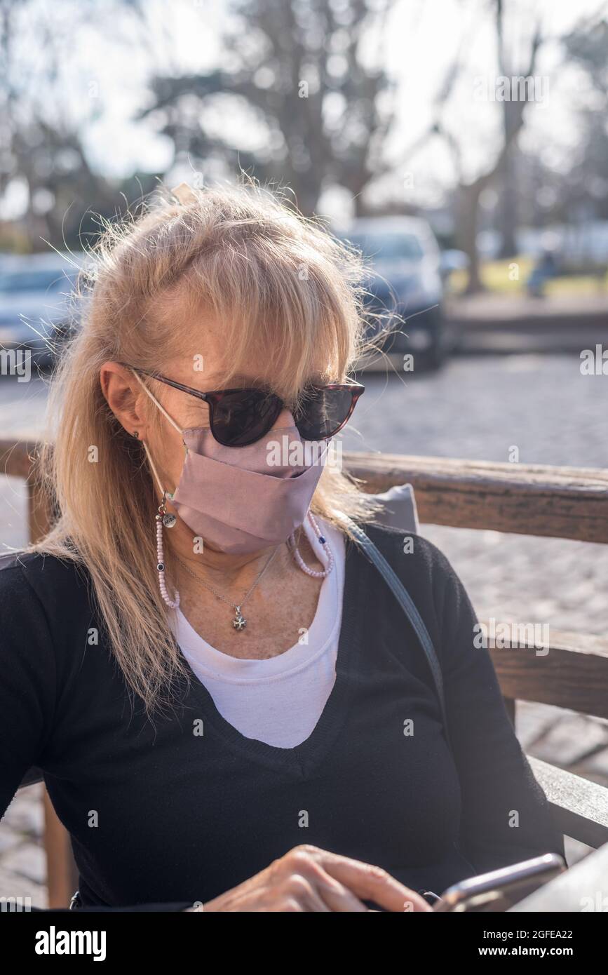 Reife Erwachsene blonde Frau lächelt mit Brille trägt Gesichtsmaske SMS auf Smartphone Stockfoto