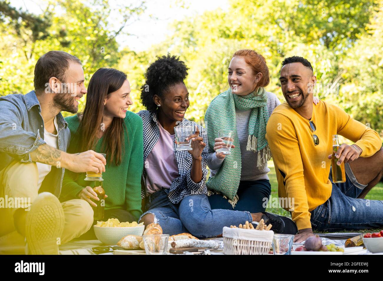 Lächelnde junge Freunde sitzen zusammen im öffentlichen Park Stockfoto