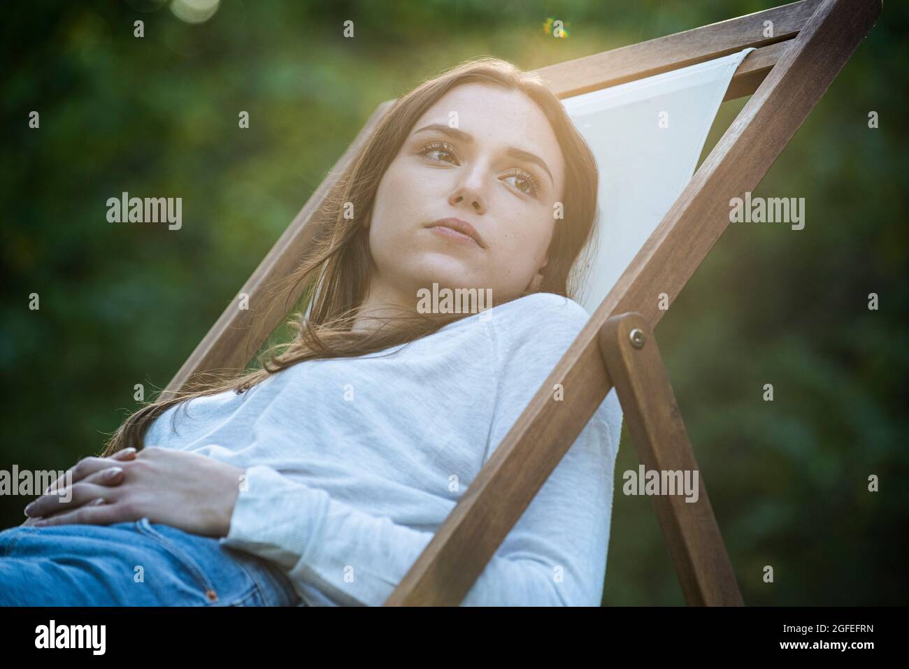 Nachdenkliche junge Frau mit Händen auf dem Bauch auf dem Stuhl gelehnt Stockfoto