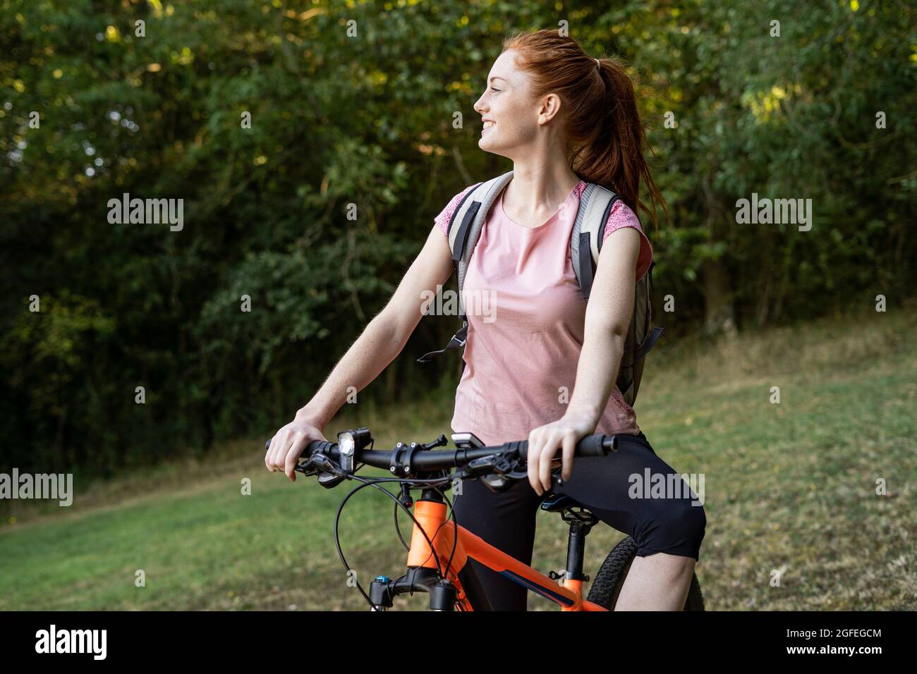Lächelnde junge Frau, die im Wald auf dem Fahrrad sitzt Stockfoto