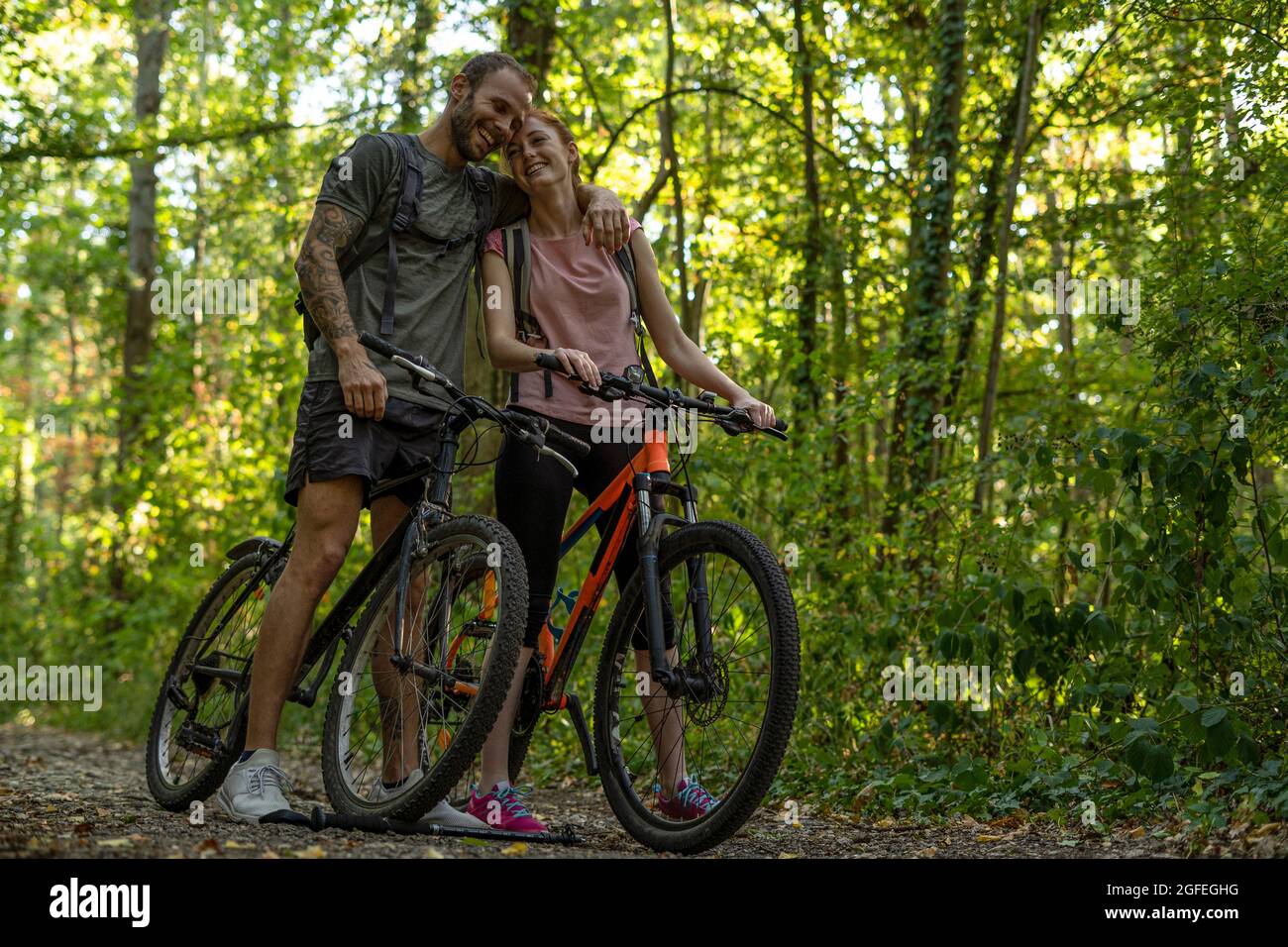 Lächelndes junges Paar, das mit Fahrrädern im Wald steht Stockfoto