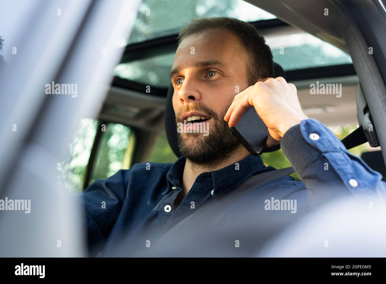 Junger Mann, der Smartphone benutzt, während er ein Auto fährt Stockfoto
